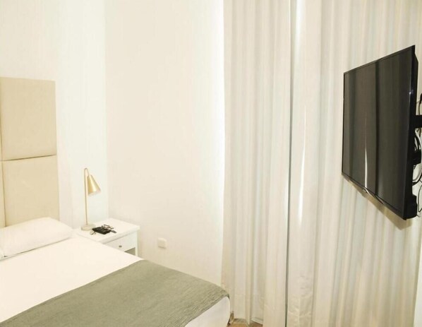 A hotel room with a bed, a bedside table, a lamp, and a TV mounted on the wall. - Casa Paracas (Paracas)