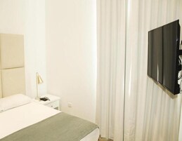 Una habitación de hotel con una cama, una mesita de noche, una lámpara y un televisor montado en la pared.