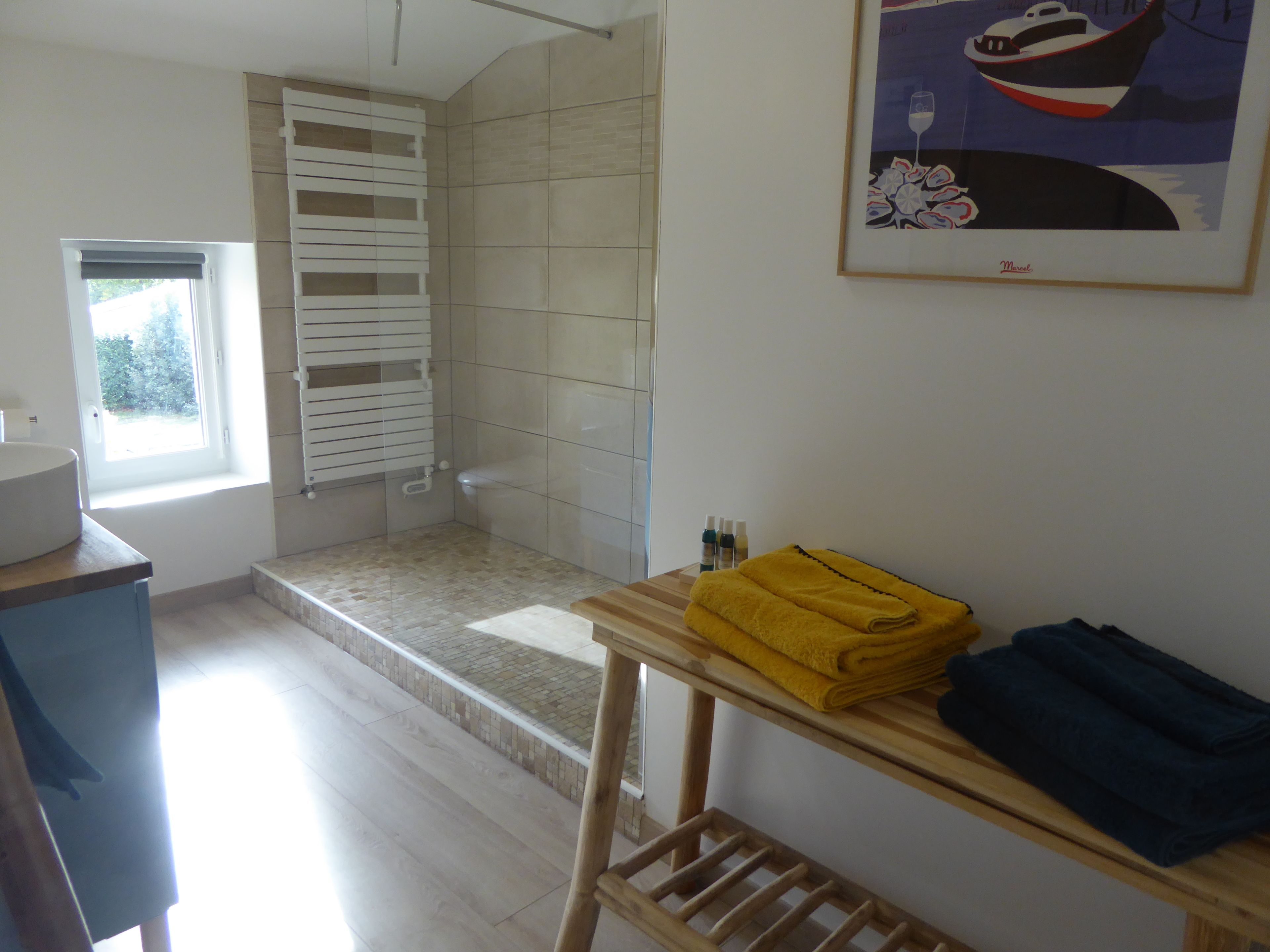 A bathroom with a shower, a window, a sink, and a towel rack with towels.