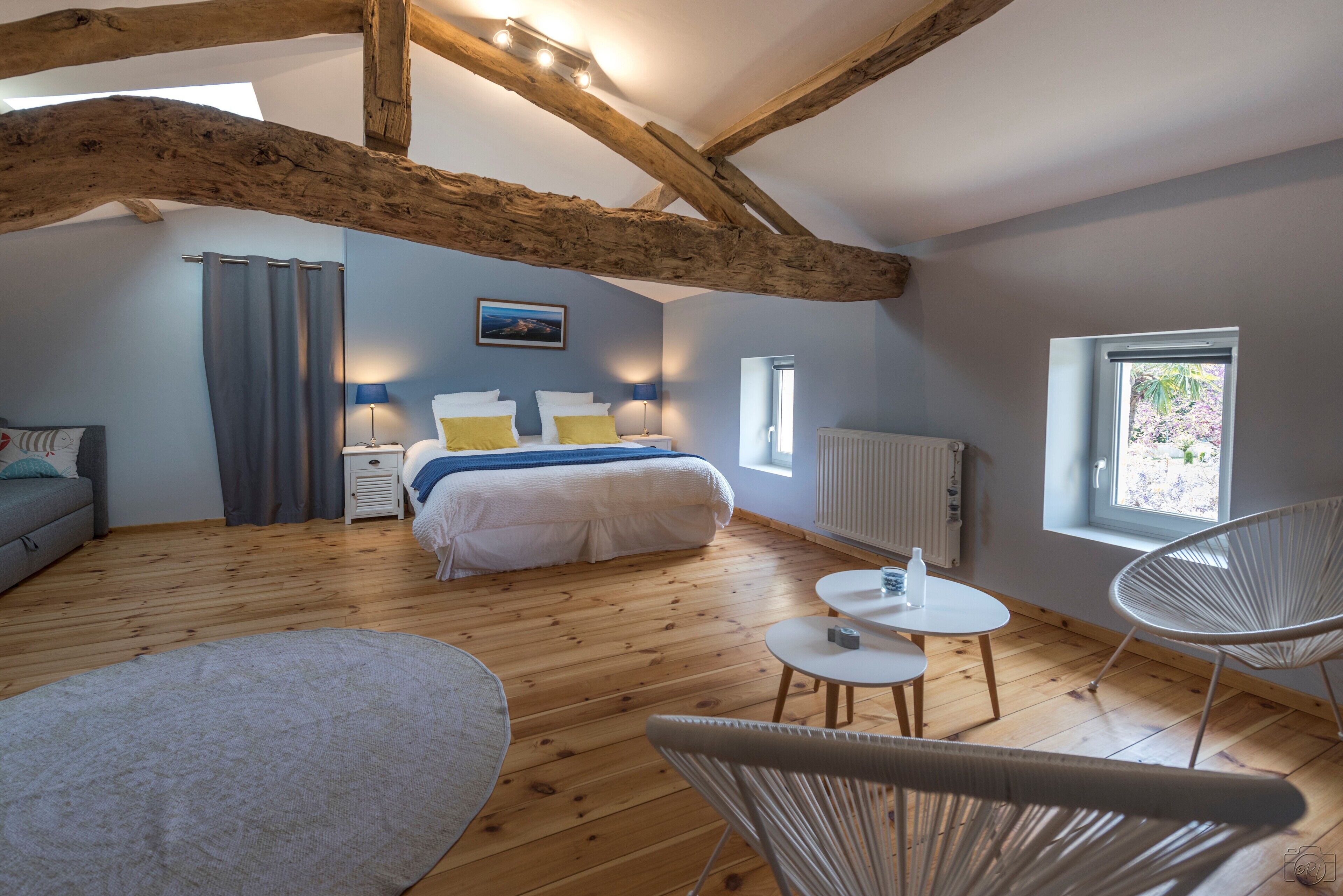 Una camera da letto con soffitto in legno, un letto con biancheria bianca, un tavolino con una bottiglia e una sedia.