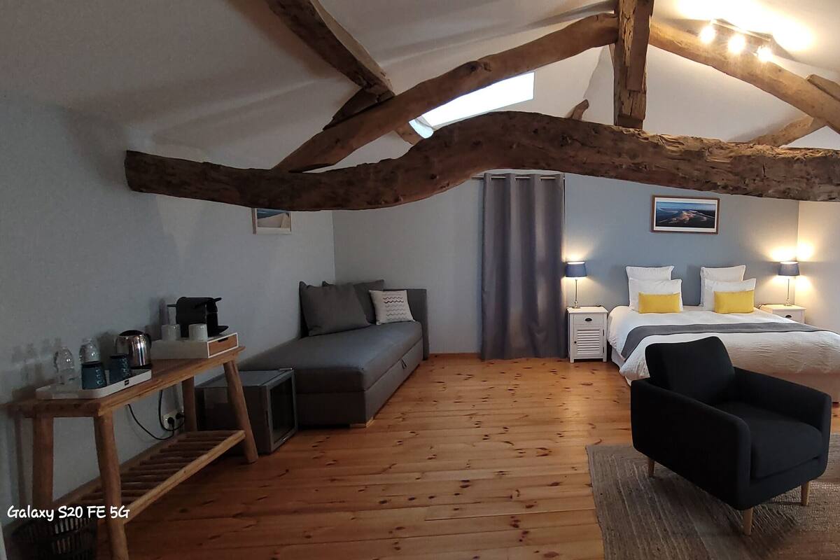A cozy bedroom with a bed, two armchairs, a small table, and a wooden floor.