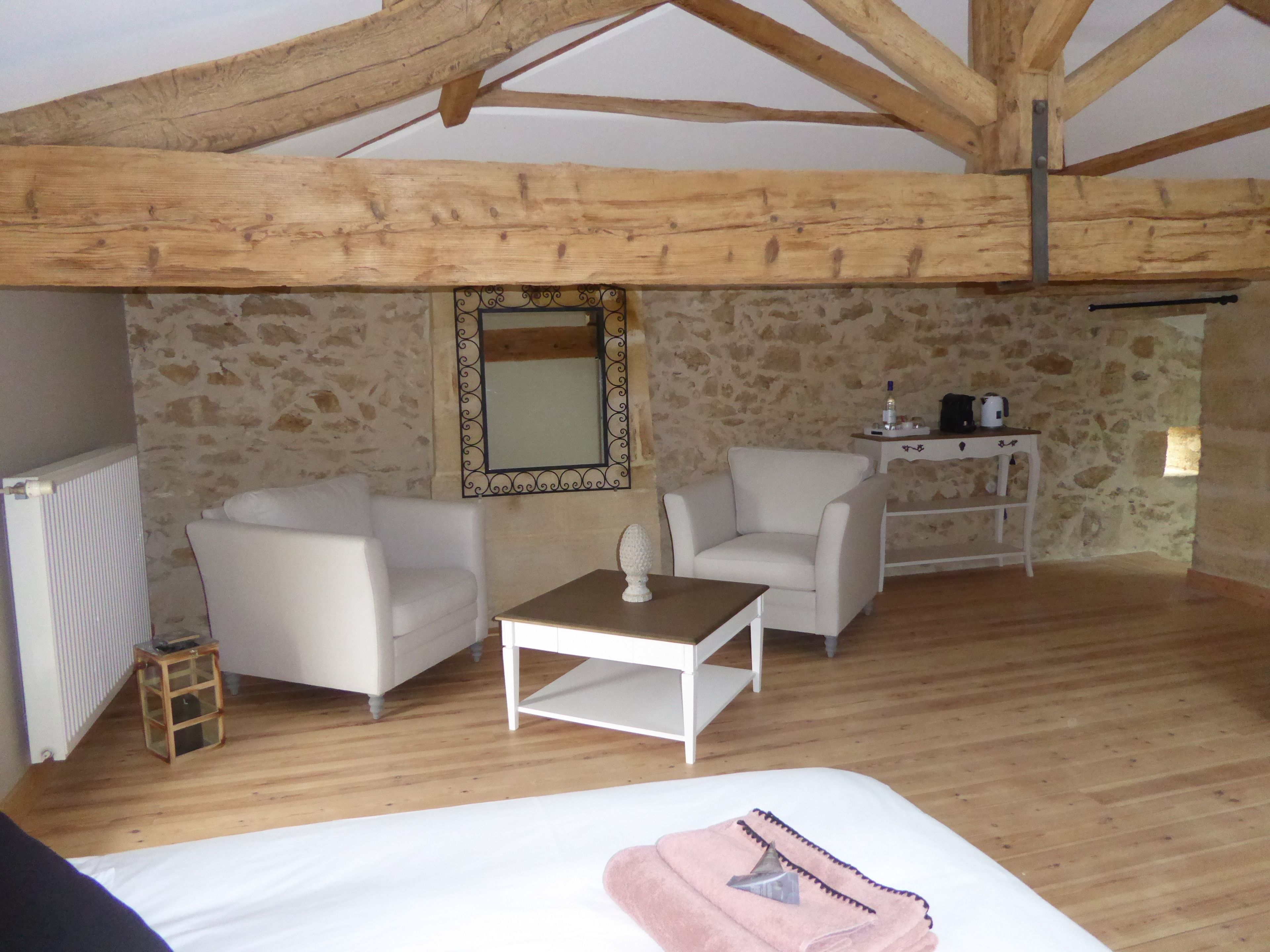 A cozy room with a bed, two white armchairs, a small table, and a stone wall with a mirror.