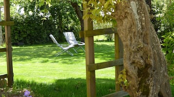 Una pérgola de madera con dos sillas de jardín blancas bajo un árbol.