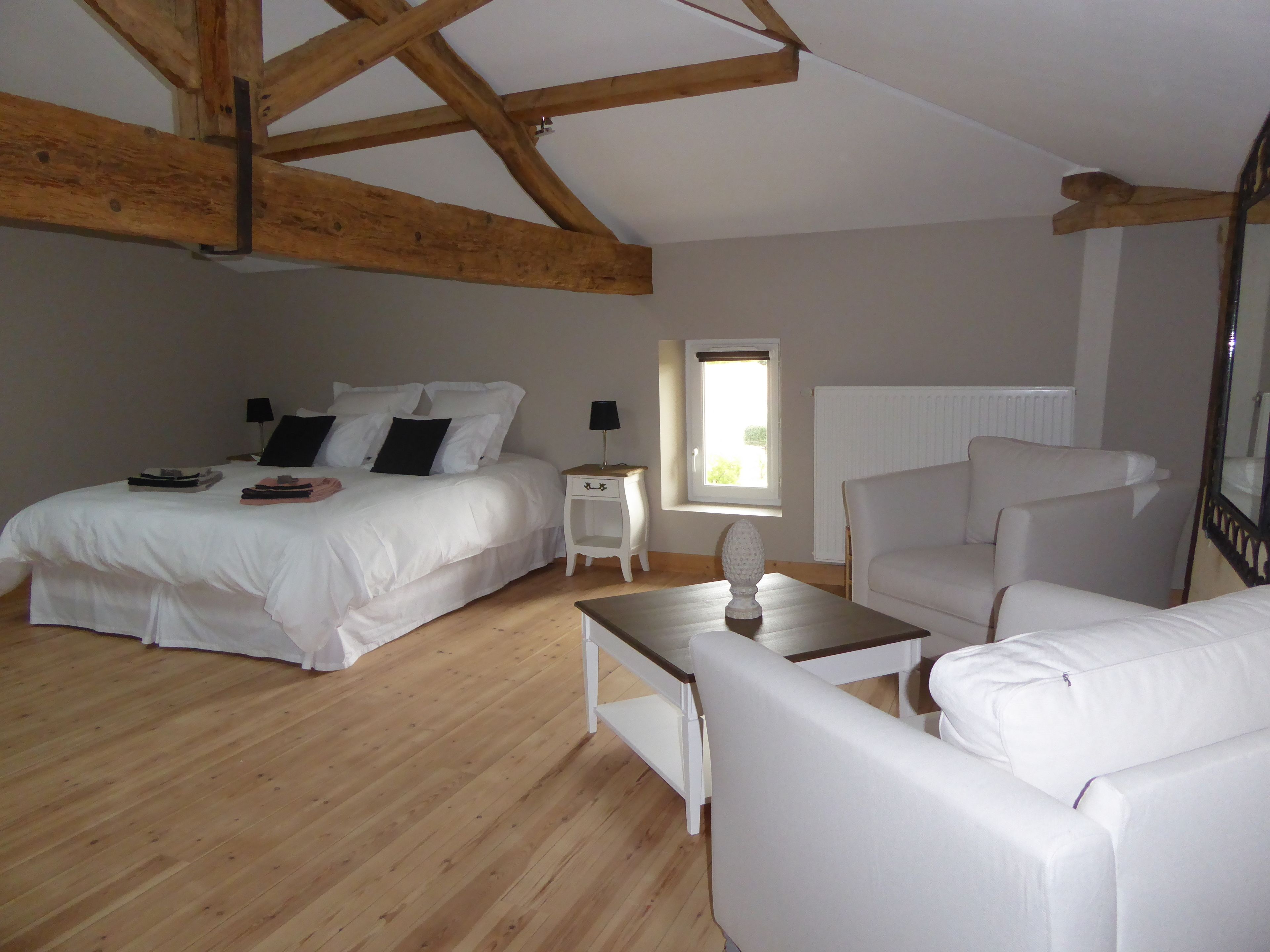 A bedroom with a large bed, a small bedside table, a white armchair, and a window with a view.