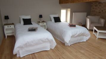 Habitació amb dos llits, terres de fusta i una paret de pedra.