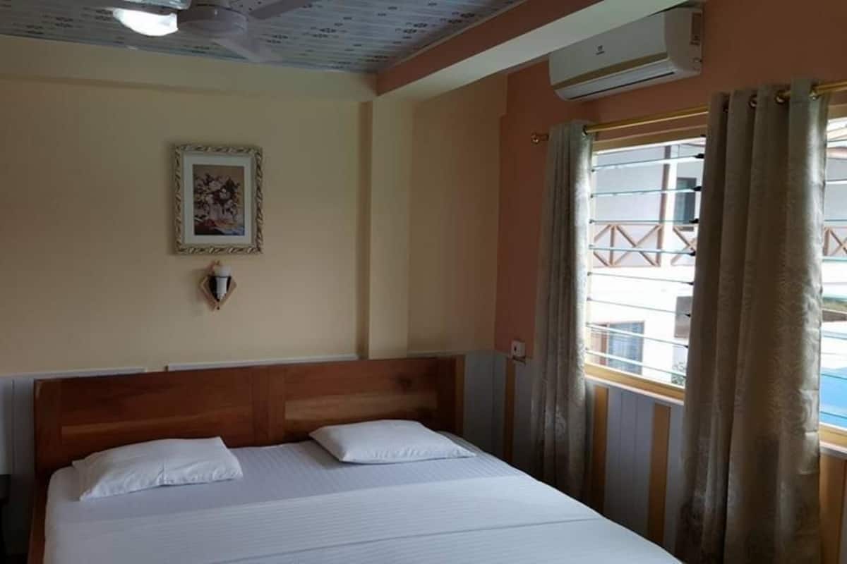 Ein Hotelzimmer mit Bett, Nachttisch, Wandlampe, einem gerahmten Bild und einem Fenster mit Vorhängen.