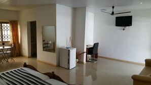 A modern hotel room with a bed, a desk, a chair, a television, and a ceiling fan. - Hans Cottage Botel (Cape Coast)