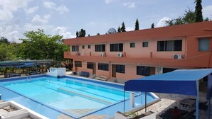 A swimming pool with a blue cover, a building with multiple windows and air conditioning units, and a clear sky. - Hans Cottage Botel (Cape Coast)