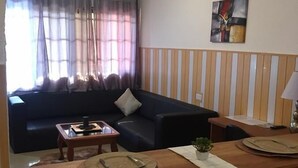 A living room with a sofa, a coffee table, and a dining area with a table set for two. - Hans Cottage Botel (Cape Coast)