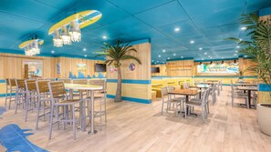 Un restaurante con decoración azul y amarilla, paneles de madera y una pantalla grande que muestra 'LANDSHARK Bar & Grill'.