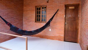 A hammock hanging between two metal bars in a room with a brick wall, a wooden door, and a window with a wooden frame. - Hotel Serrano (Martins)