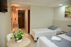 A hotel room with two beds, a small table with a vase of flowers, and a painting on the wall. - Hotel Serrano (Martins)