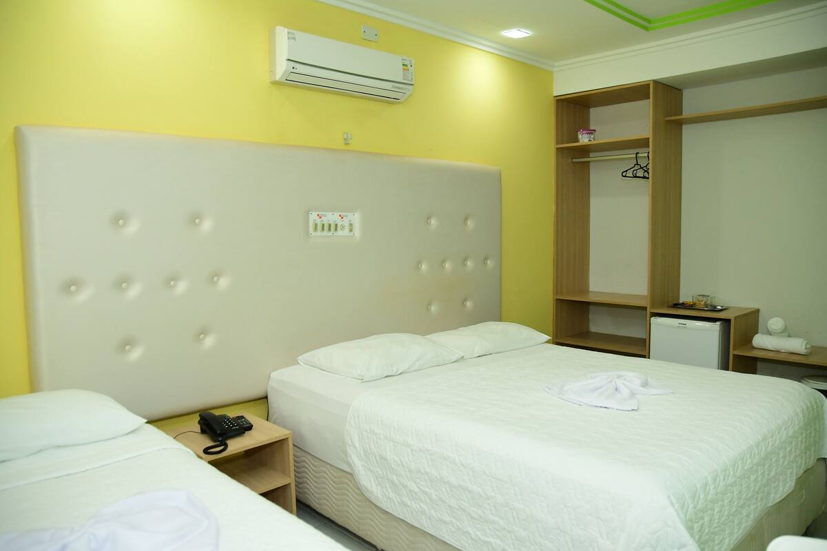 A hotel room with a large bed, a bedside table with a phone, an air conditioner, and a wardrobe.