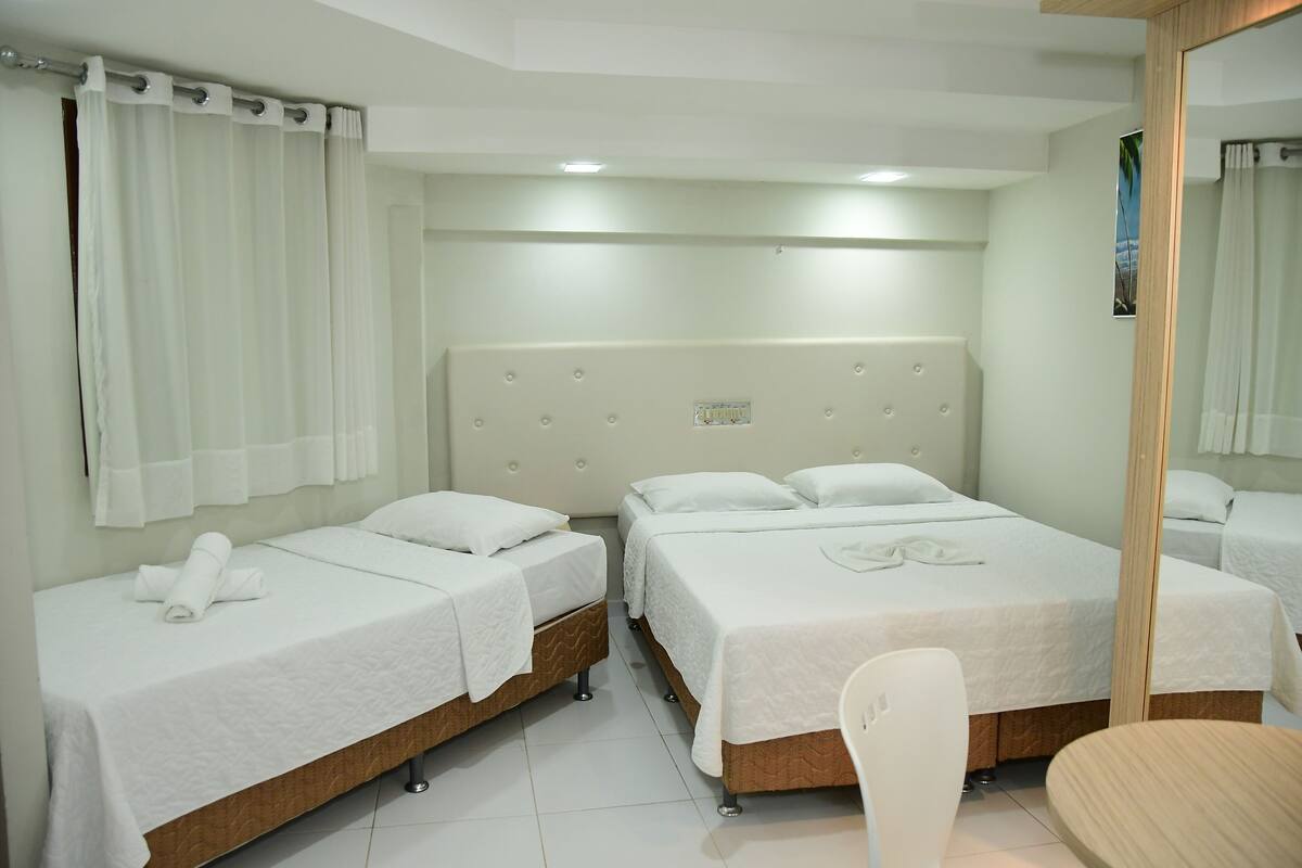 A hotel room with two single beds, a wooden headboard, a white chair, and a small table.