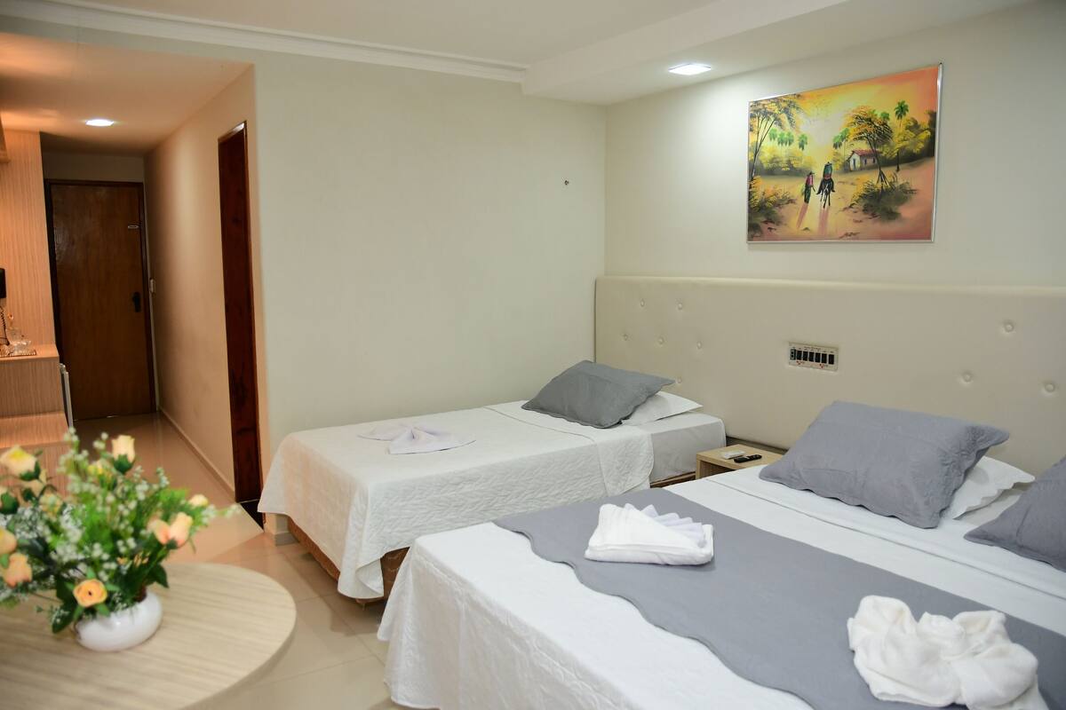 A hotel room with two single beds, a small table with a vase of flowers, and a painting on the wall.
