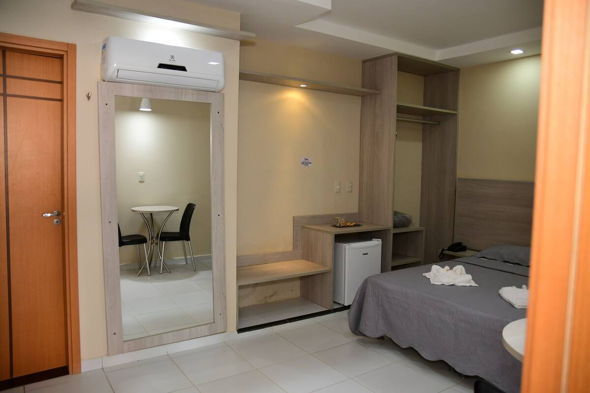 A hotel room with a bed, a desk, a chair, a small refrigerator, and a closet.
