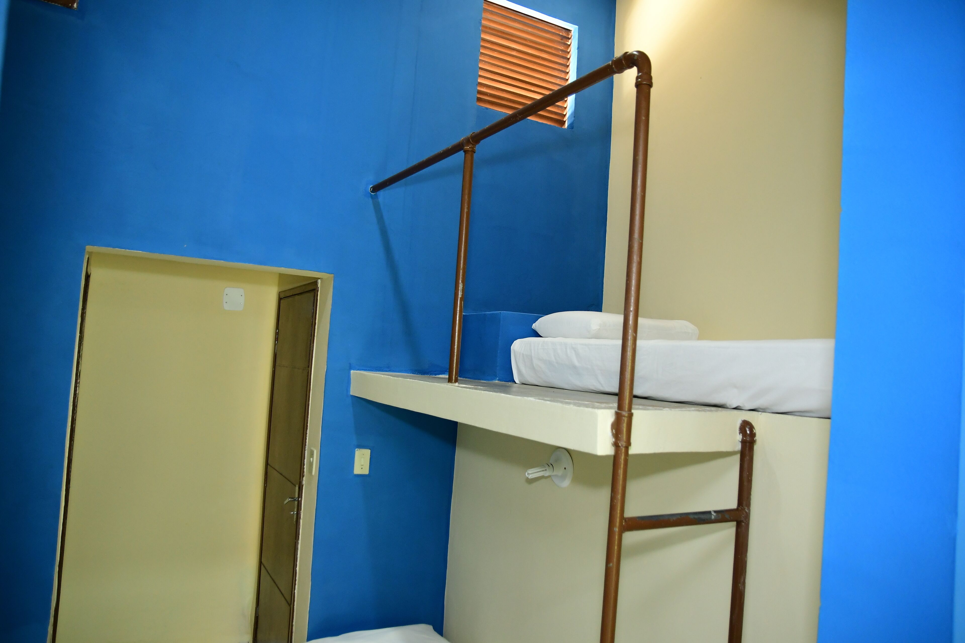 A bunk bed with a wooden ladder, a white mattress, and a window with blinds.