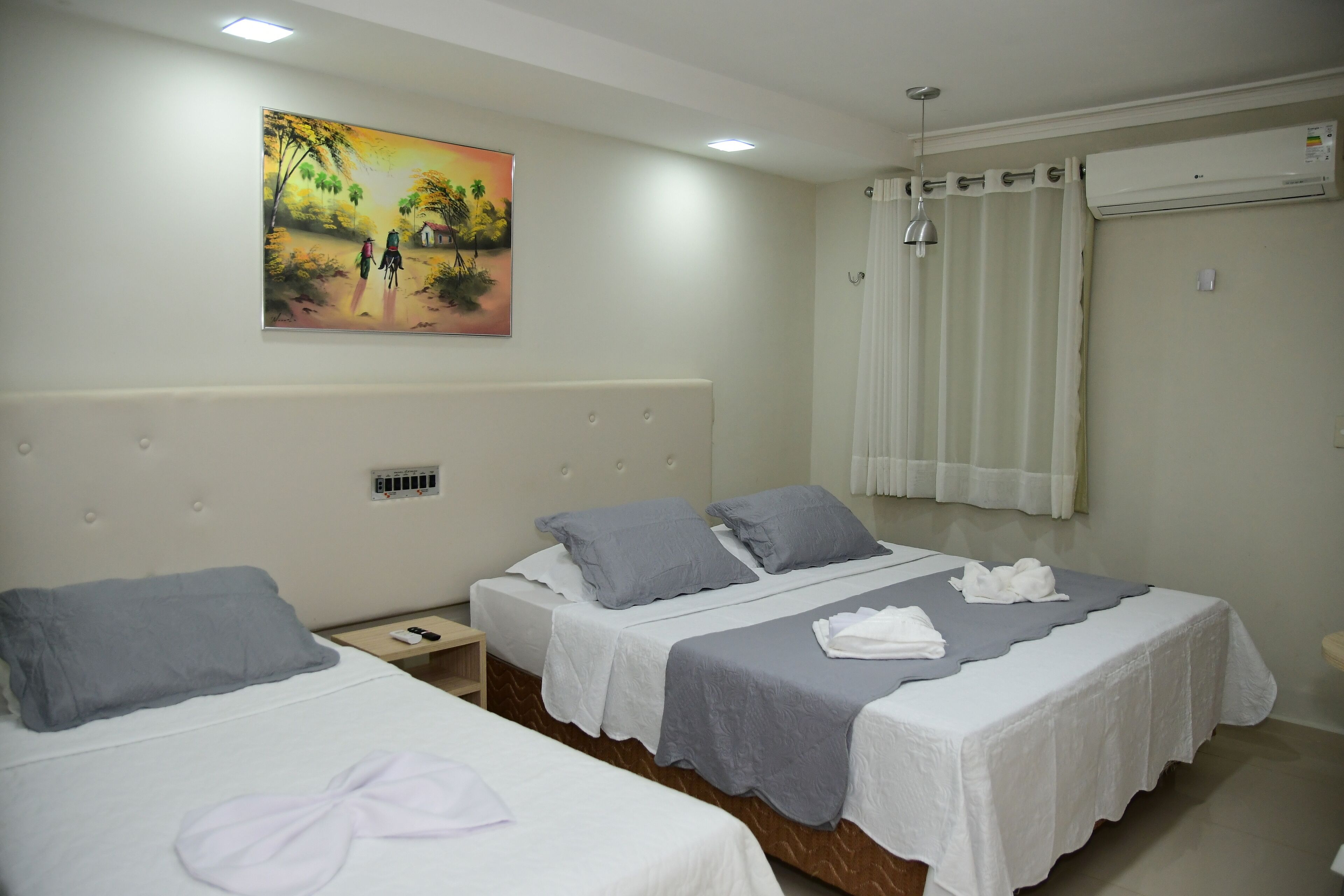A hotel room with two beds, a painting on the wall, an air conditioning unit, and a window with curtains.
