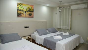 A hotel room with two beds, a painting on the wall, an air conditioning unit, and a window with curtains.