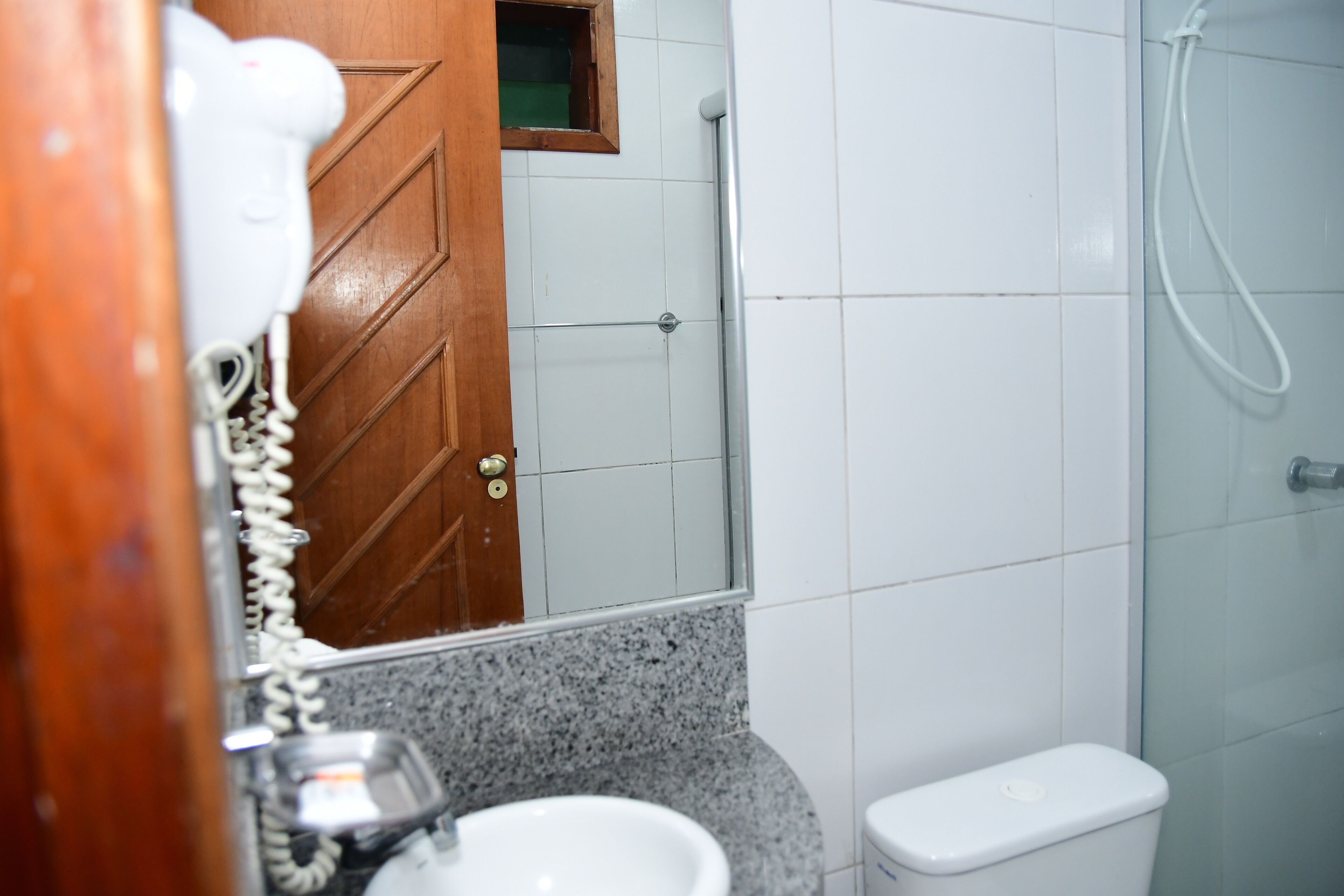 A bathroom with a wooden door, a white toilet, a sink, and a shower area.
