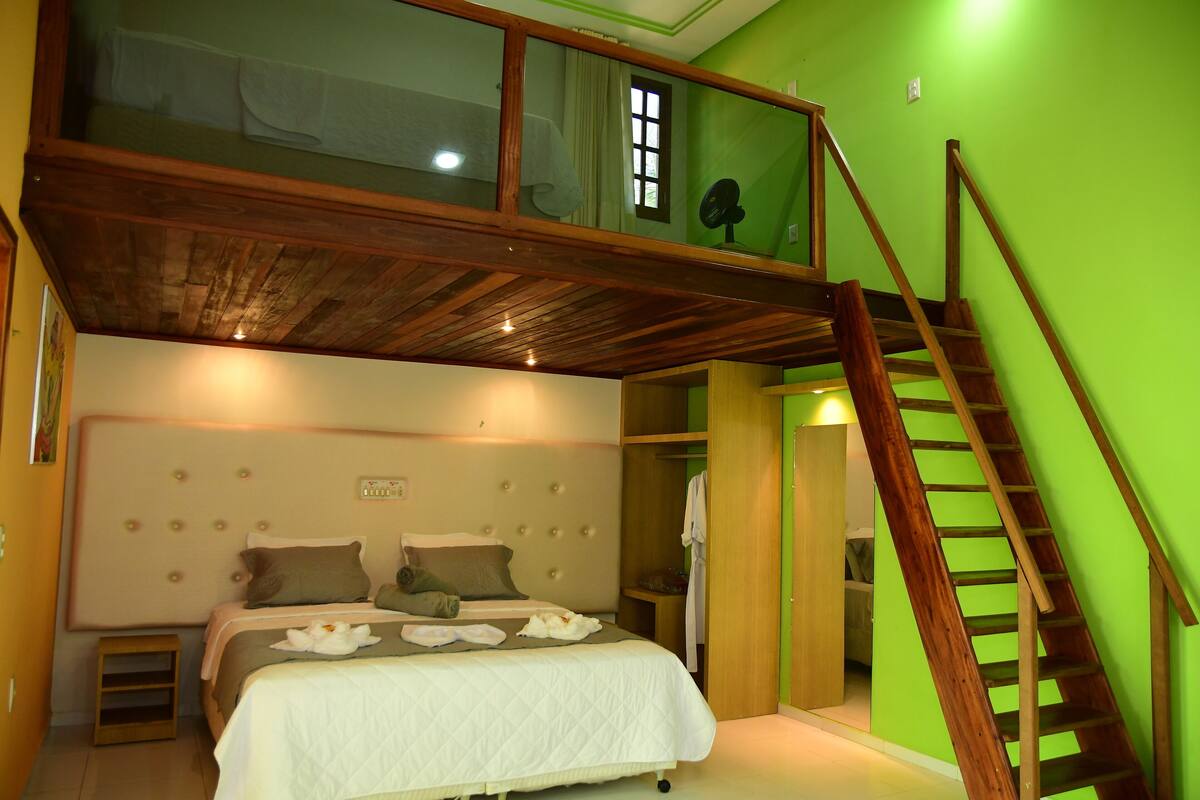 A bedroom with a loft bed, a wooden staircase, and a green wall.