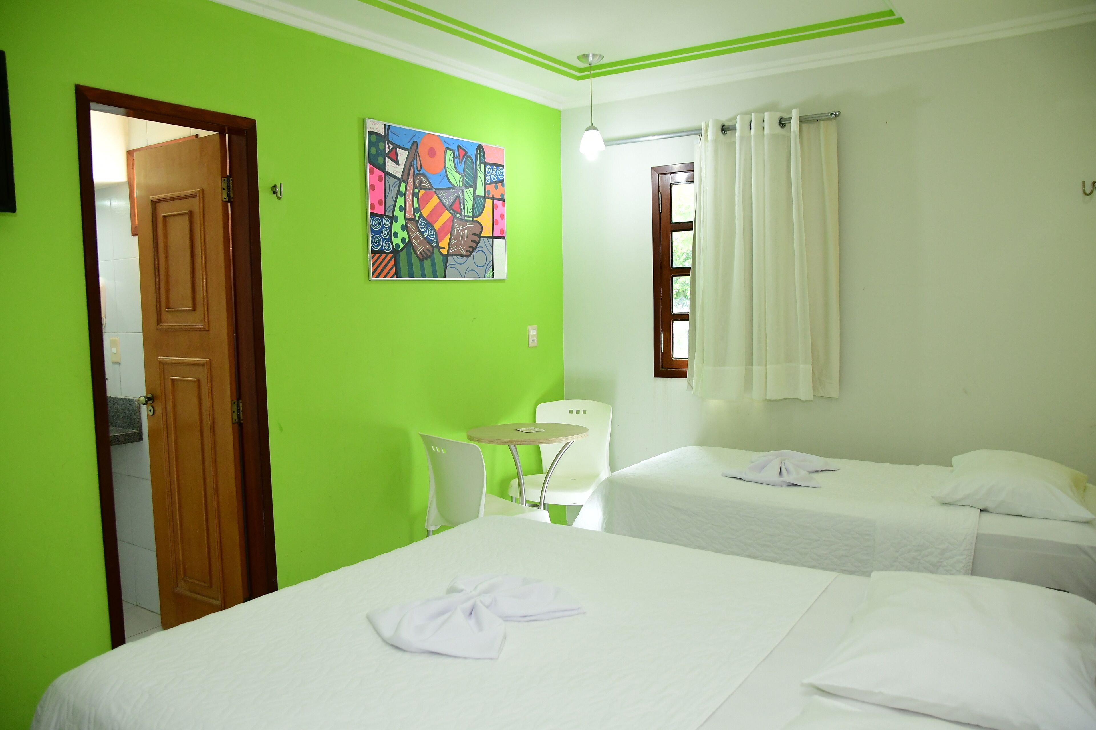 Habitación de hotel con dos camas, una mesita, una silla y un cuadro de colores en la pared.