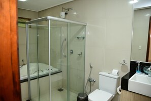A modern bathroom with a glass-enclosed shower, a white bathtub, and a sink with a black countertop. - Hotel Serrano (Martins)