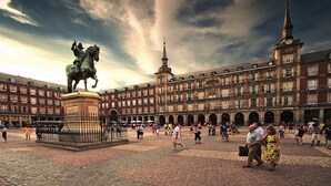 Una plaza histórica con una estatua de una figura a caballo, rodeada de arquitectura clásica y una multitud de personas.