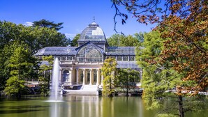 A large glass-domed building with a fountain in front, surrounded by trees and a body of water. - La Reina de Gran Via (Madrid)