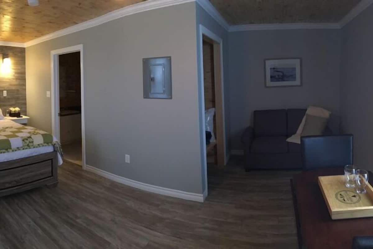 Une chambre à coucher comprenant un lit, des tables de chevet, une commode, un plafond en bois et un petit coin salon avec une table et des chaises.
