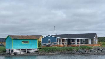 Waterfront property with three buildings, each with a unique design, situated over the water and surrounded by lush vegetation and a rocky shoreline.