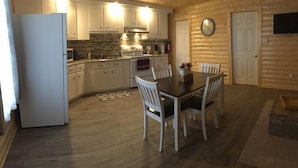 A compact kitchen with white cabinets, a microwave, and a stove. There is a dining table with four chairs and a clock on the wall.
