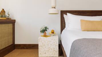 A neatly arranged bedroom with a bed, bedside table, and a small side table with a vase and fruit.