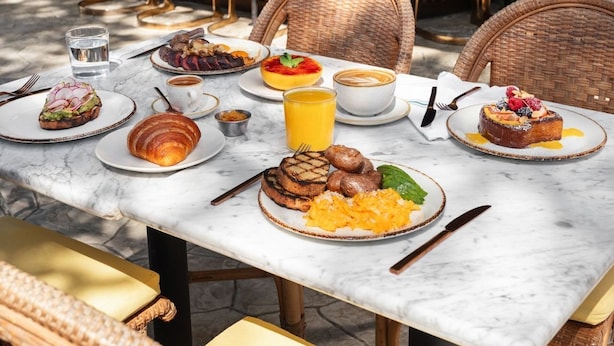 A breakfast table with plates of food, a glass of orange juice, and a croissant. - Silver Lake Pool & Inn (Los Angeles)