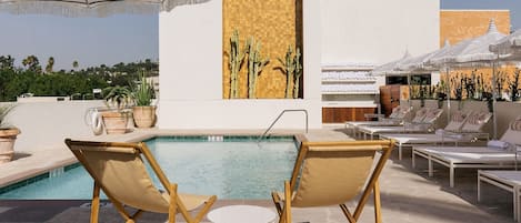 Una piscina al aire libre, sombrillas, sillones reclinables de piscina