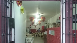 A narrow hallway with a red and white color scheme, leading to a dining area with plastic chairs and tables. - Hostal El Exito (Santa Marta)