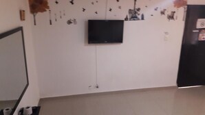 A room with a mounted television on the wall, a door on the right, and a wall with various stickers. - Hostal El Exito (Santa Marta)