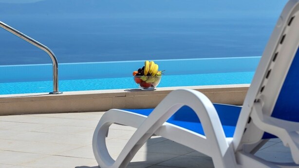 A poolside view with a clear blue sky, a white chair, and a bowl of fruit. - Villa Makar with  infinity heated pool,gym,grill, 3 bedrooms,3 bathrooms (Dalmatia)
