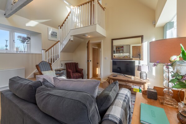 A spacious living room with a high ceiling, a staircase, a comfortable sofa, a wooden coffee table, and a television.