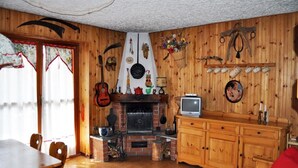 A cozy living room with a fireplace, wooden walls, a television, and a dining area with a table and chairs. - Rustic in the Chapelle complex (Sauze d` Oulx)