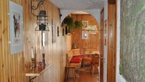 A wooden hallway with a patterned rug, a dining area with a red tablecloth, and a hanging plant. - Rustic in the Chapelle complex (Sauze d` Oulx)