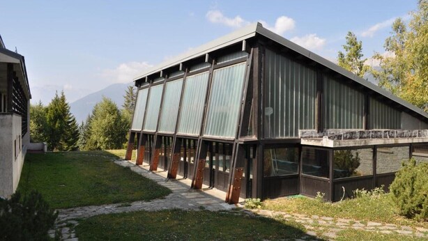 A modern building with a sloped roof, large windows, and a stone pathway leading to the entrance. - Rustic in the Chapelle complex (Sauze d` Oulx)