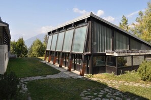 A modern building with a sloped roof, large windows, and a stone pathway leading to the entrance. - Rustic in the Chapelle complex (Sauze d` Oulx)