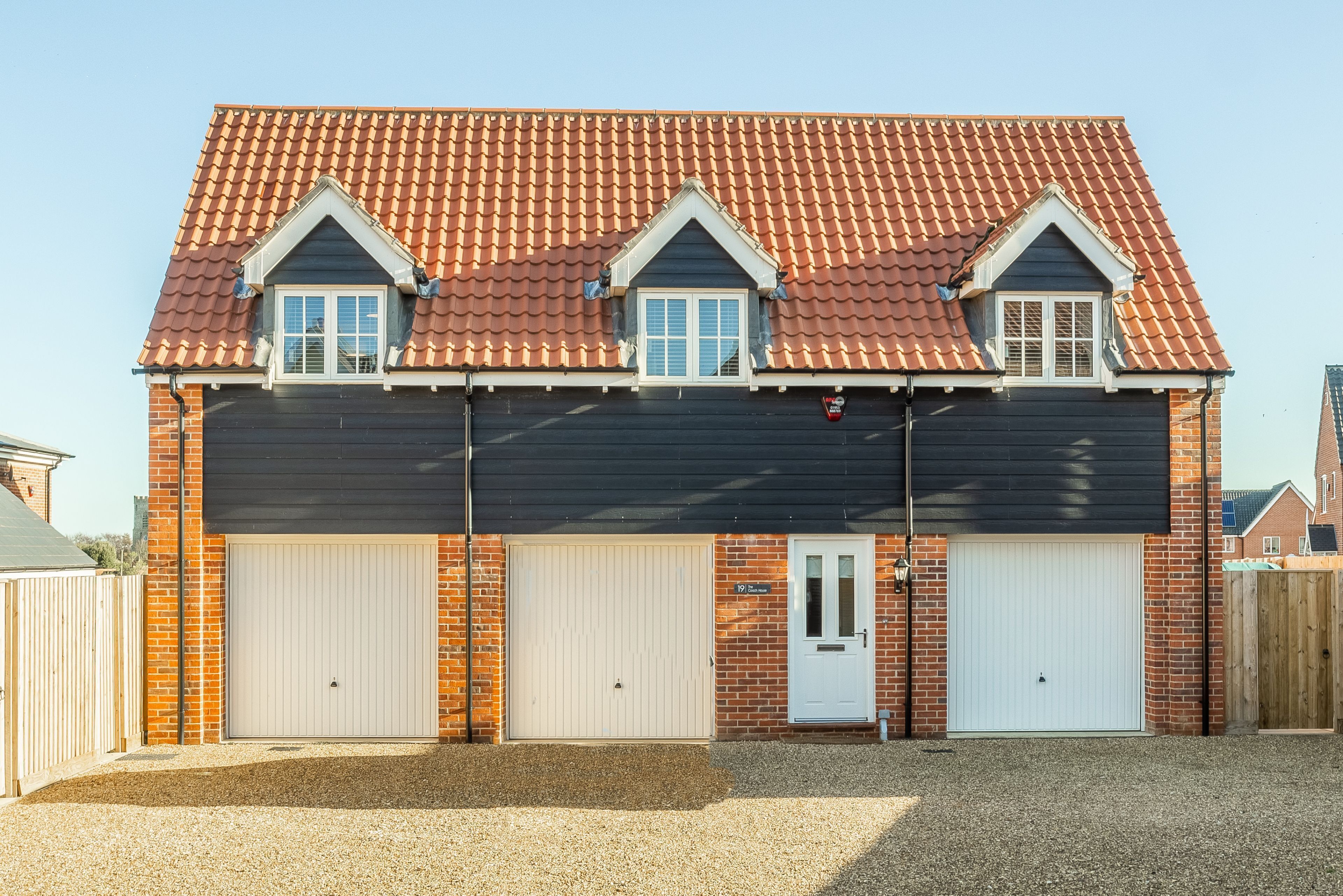 Une maison à deux étages, avec un toit en tuiles, deux portes de garage et une façade en briques.