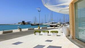 A marina with boats, a covered seating area with planters, and a building with large windows. - Levante, Holiday Home 100 metres from the sandy beach and near the centre (Marina di Ragusa)