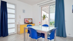 A modern dining area with a glass table, blue chairs, a yellow cabinet, and a television on a stand. - Levante, Holiday Home 100 metres from the sandy beach and near the centre (Marina di Ragusa)