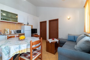 Espaço compacto para vivenciar, com mesa de jantar, cadeiras, sofá, televisão e cozinha equipada com frigor ífico, micro-ondas e armários.