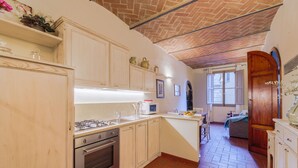 A kitchen with wooden cabinets, a gas stove, an oven, and a microwave. There is a window with open shutters and a door leading to another room. - Beautiful apartment for 4 guests with WIFI, A/C, TV and pets allowed (Cortona)