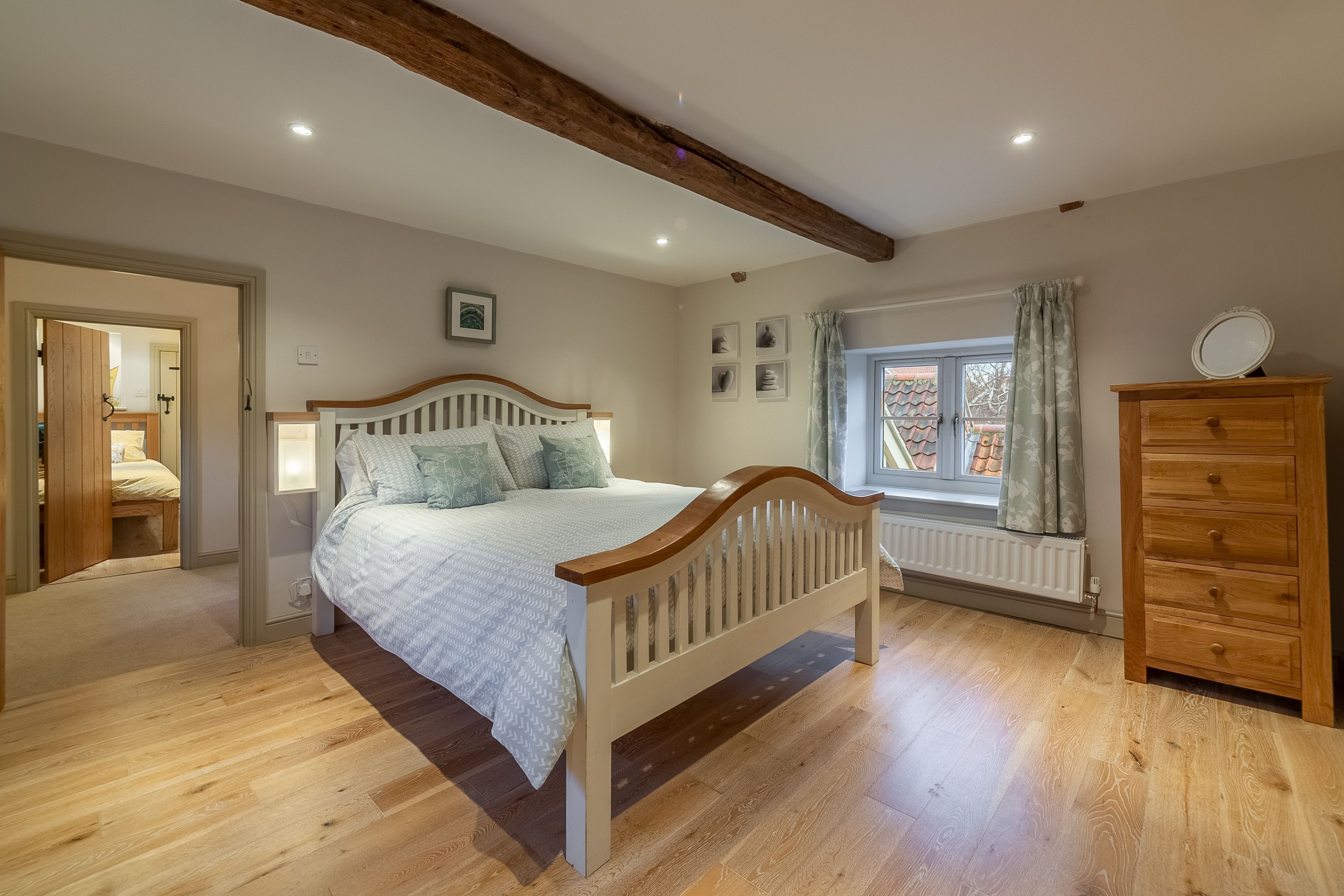 A bedroom with a wooden bed, a dresser, and a window with curtains.