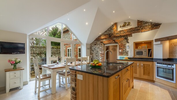 A modern kitchen with a large island, stone accents, and a stone wall. - Mayes Cottage, Brancaster, Norfolk (Brancaster)